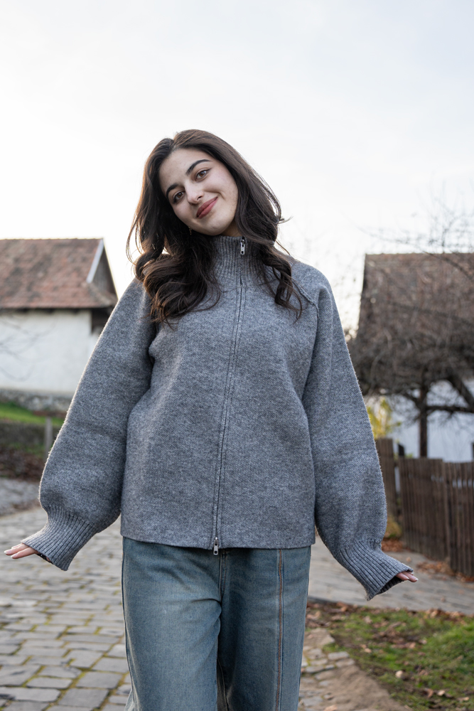 Lila smiling during a VIP Transformational Empowerment Photoshoot in Hollókő, Hungary, wearing a cozy grey sweater on a cobbled street.